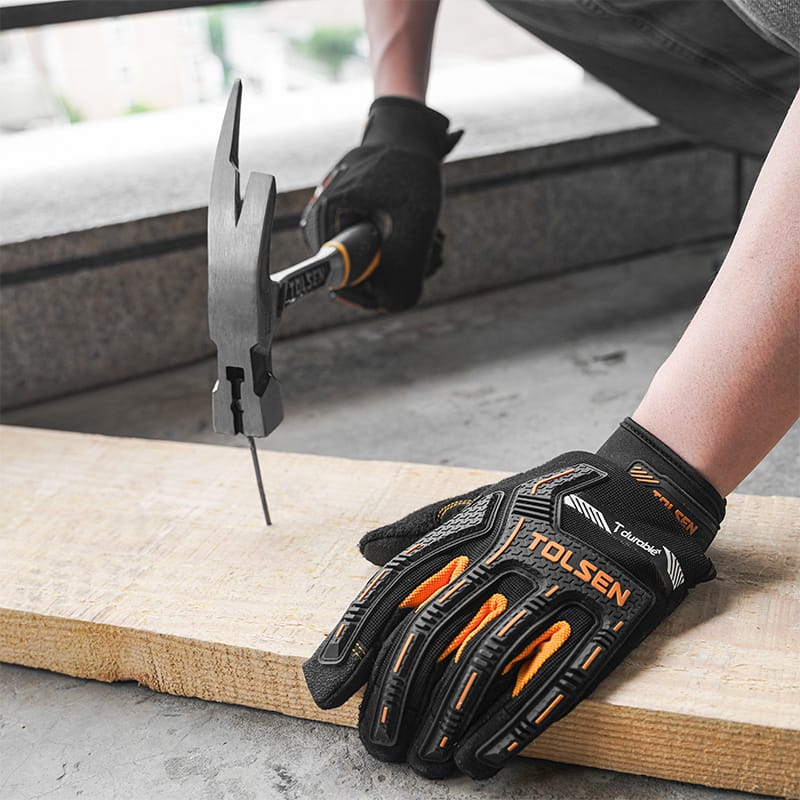 Gloved hand driving a nail into a wooden plank with a Tolsen one-piece forged roofing hammer