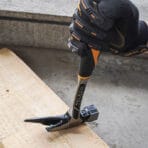 Gloved hand using the Tolsen one-piece forged roofing hammer to pull a nail from wood