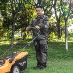 Man wearing Tolsen work jacket while operating a lawn mower for landscaping and outdoor tasks.