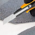 Tolsen snap-off blade utility knife cutting through grey carpet material with precision.