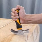 Close-up action shot of a hand using the Tolsen claw hammer to drive a nail into a wooden board.