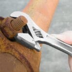 Tolsen adjustable wrench being used to tighten a large bolt on a rusty metal pipe.