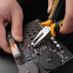 Close-up of hand using Tolsen 4.5 inch mini long nose pliers to work on a circuit board