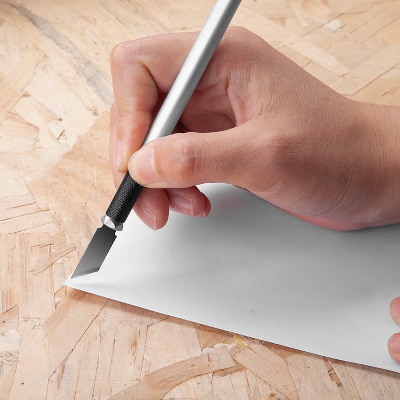 Hand using a Tolsen precision hobby knife to cut paper on a wooden surface