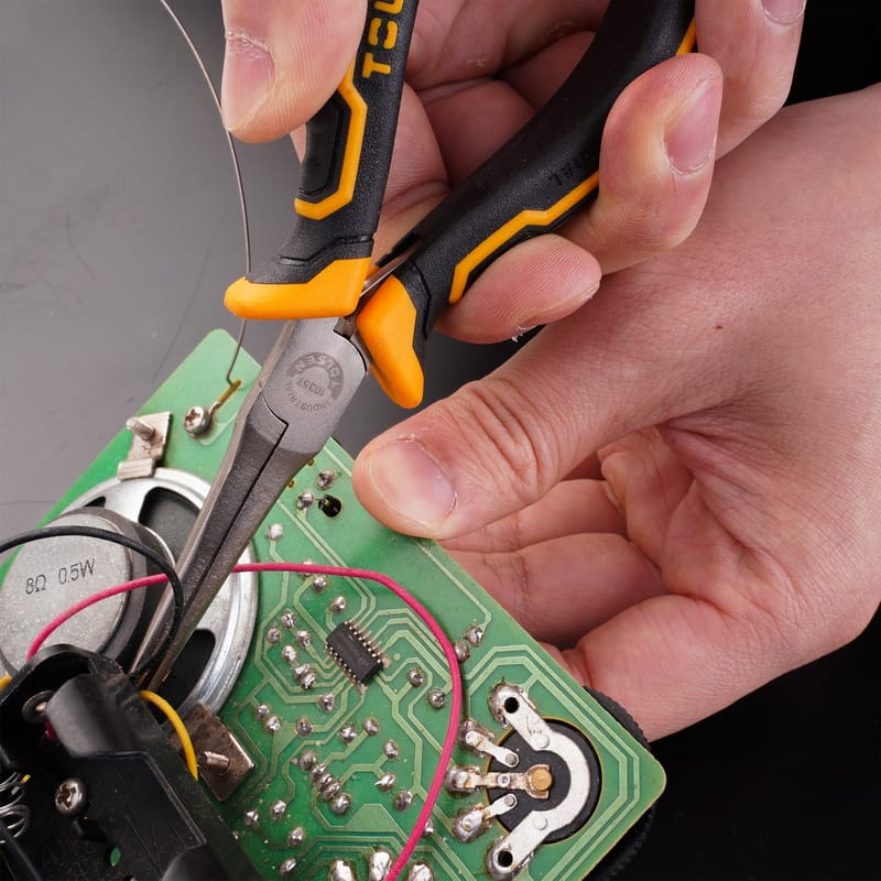 Technician using Tolsen long nose pliers to work on a green electronic circuit board assembly.