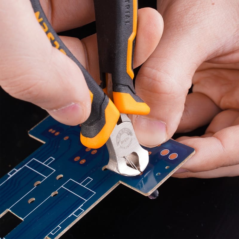 Close-up of Tolsen end cutting pliers being used to trim component legs on a blue printed circuit board.