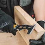Close-up of a Tolsen multi-purpose putty knife scraping or shaping wood