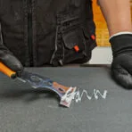 Gloved hand removing caulk or sealant with a Tolsen 14-in-1 putty knife