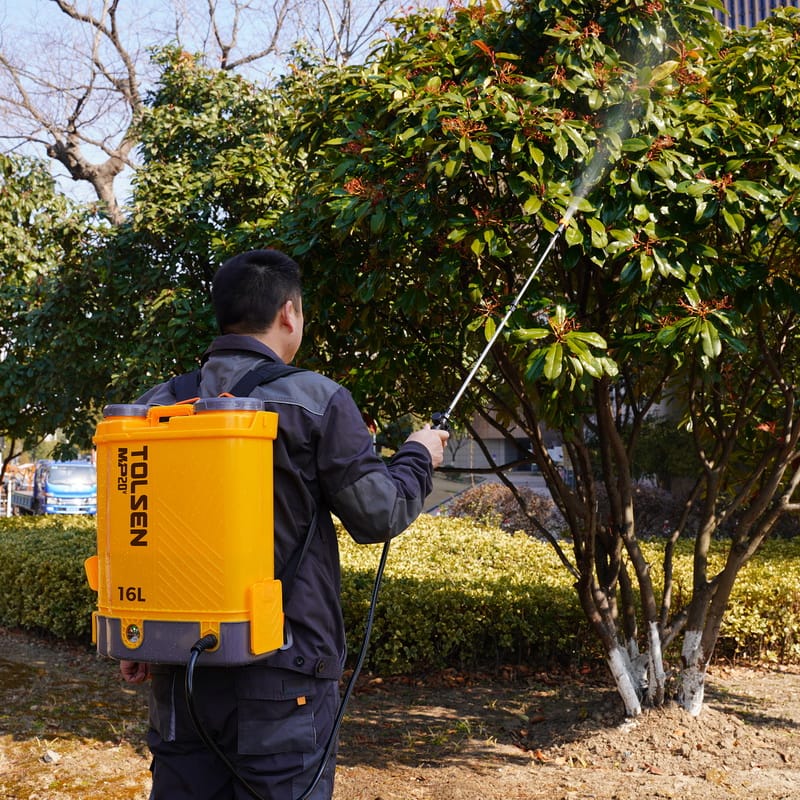 Person using TOLSEN 20V Cordless Backpack Sprayer to treat tree foliage with liquid spray in a garden setting