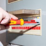 Electrician using Tolsen 1000V insulated screwdriver to safely tighten terminal screws in a circuit breaker panel.