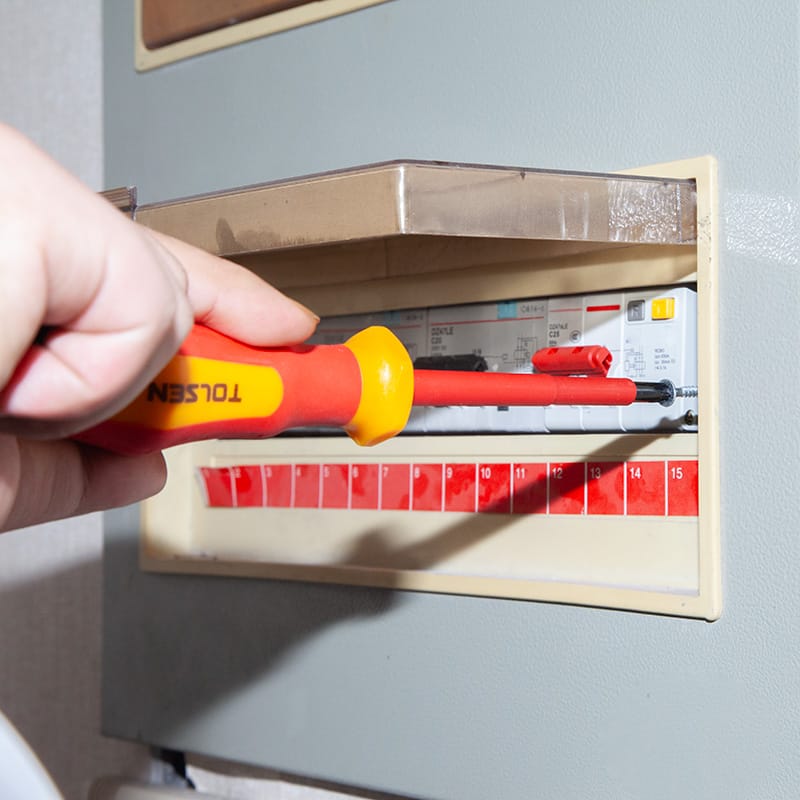 Electrician using Tolsen 1000V insulated screwdriver to safely tighten terminal screws in a circuit breaker panel.