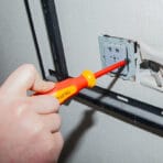 Hand using a Tolsen VDE safety screwdriver to install a wall power socket faceplate.