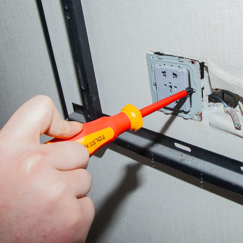 Hand using a Tolsen VDE safety screwdriver to install a wall power socket faceplate.