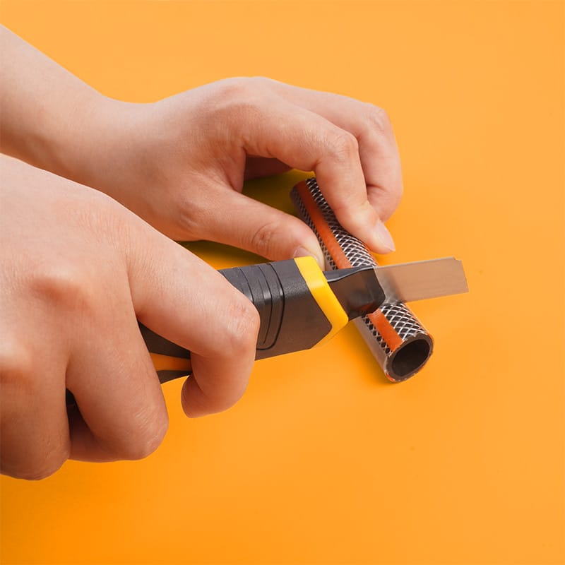 Tolsen heavy-duty snap-off knife cutting through a reinforced plastic hose, demonstrating cutting force and durability.
