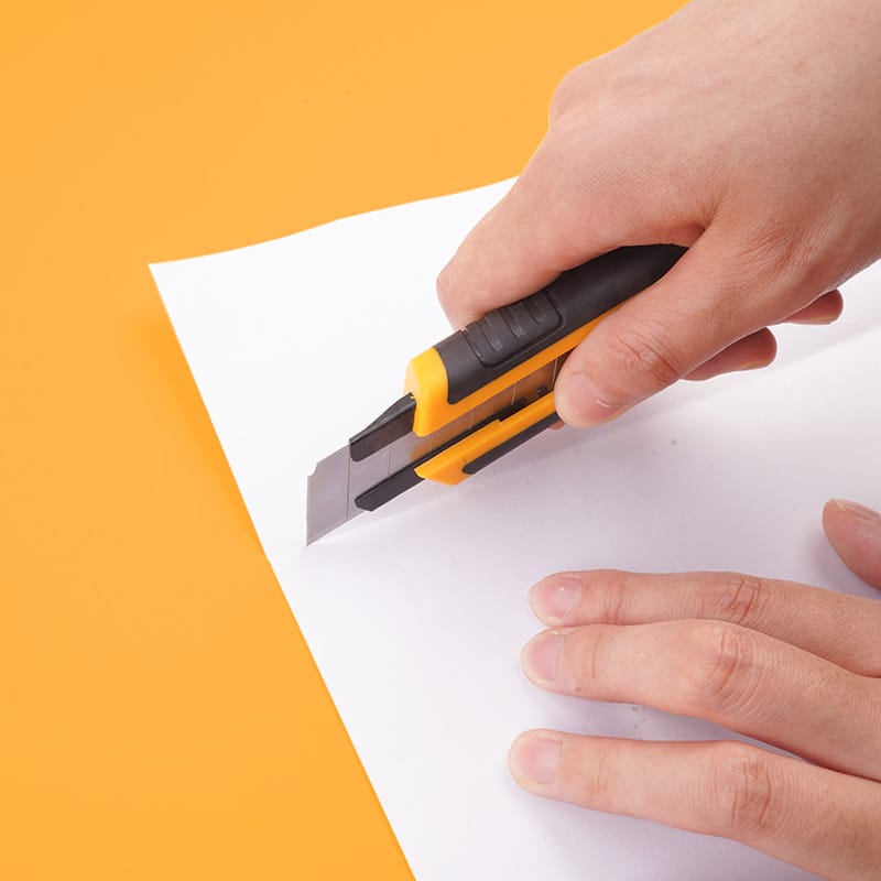 Hand using Tolsen snap-off blade knife to precisely cut a sheet of white paper demonstrating blade sharpness.