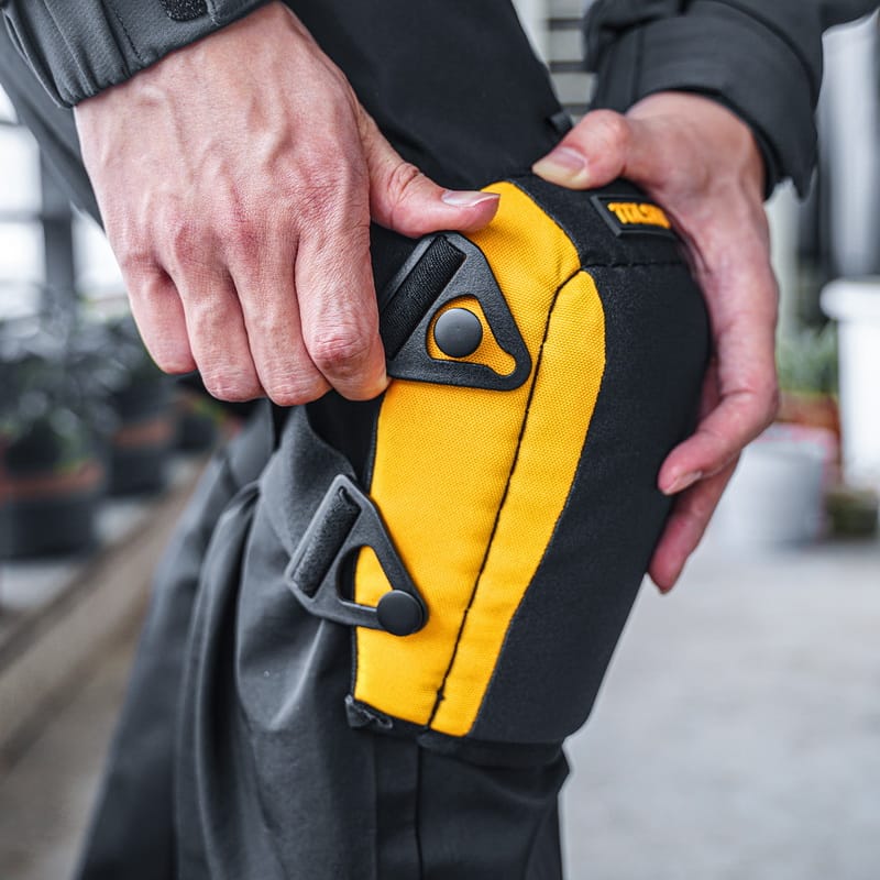 Close-up view of a worker's hands adjusting the side buckle and strap on the TOLSEN knee pad to ensure a secure and comfortable fit on the leg.