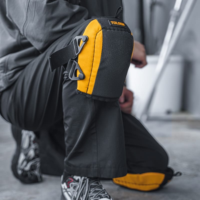 A construction worker kneeling on a concrete floor wearing TOLSEN heavy-duty knee pads, demonstrating comfortable knee protection during work.